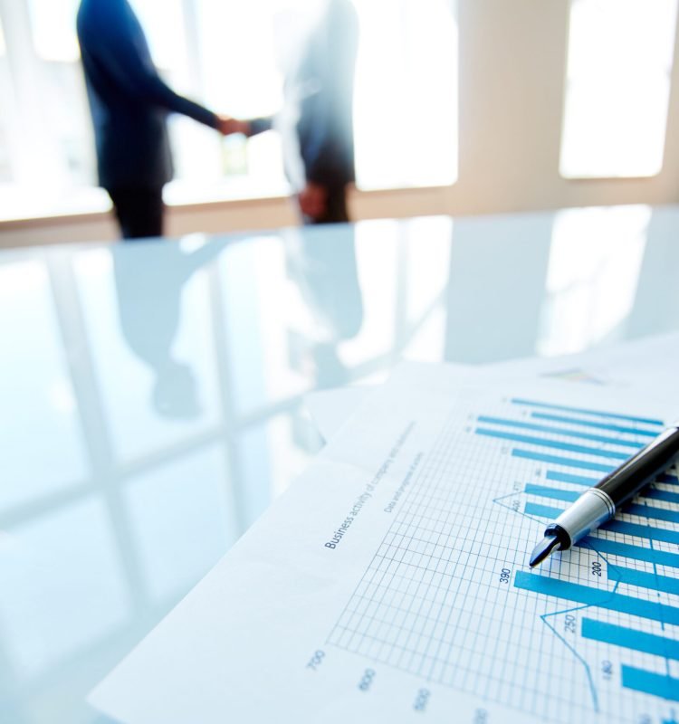 Business documents with charts on the table with business people in the background