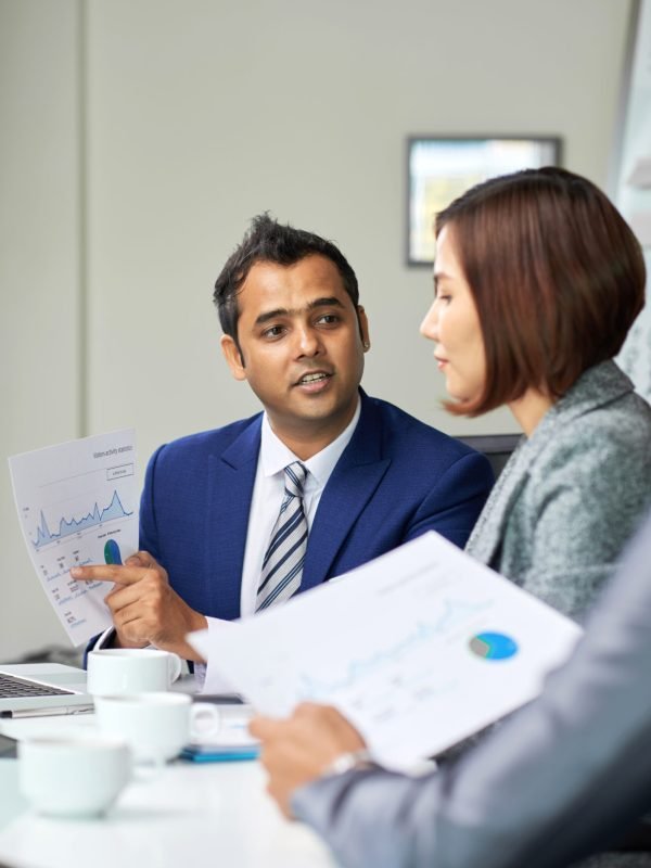 Confident businessman sitting at meeting and discussing financial diagram together with his coworkers